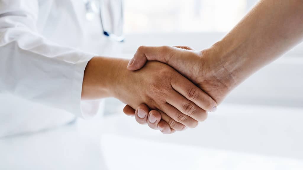 Female doctor shaking hands with man in medical office