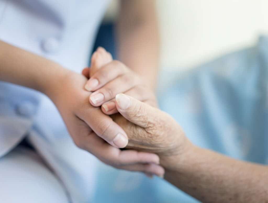 Nurse sitting on a hospital bed next to an older woman helping hands, care for the elderly concept