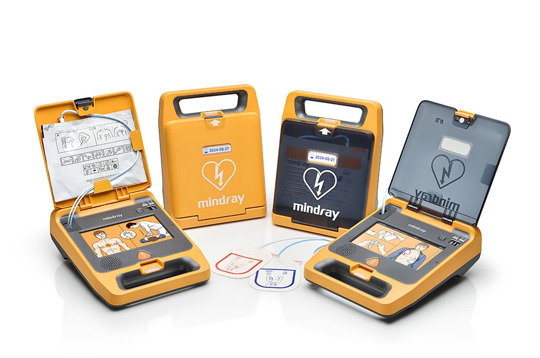 Drei AED-Geräte in Orange, offen mit Anleitungen und Elektroden, auf einer weißen Fläche.